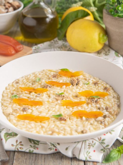 Risotto all'olio con vongole, bottarga e limone guarnito con lamelle di bottarga e foglie di basilico