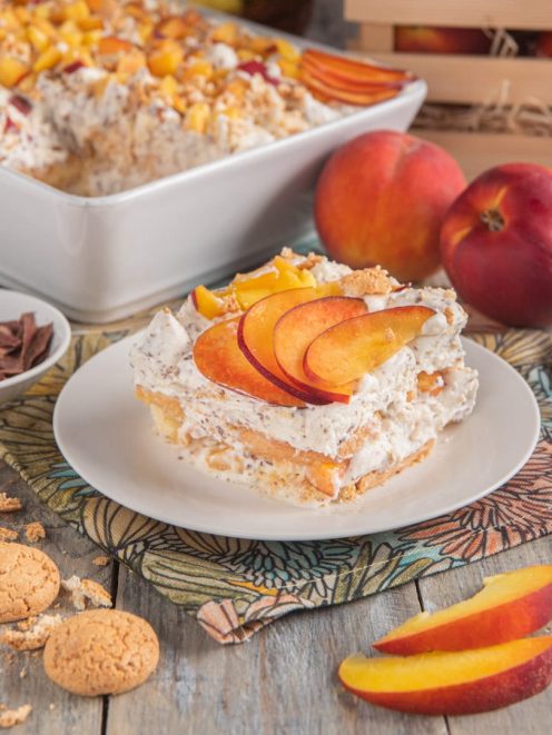 Tiramisù con pesche e amaretti servito a fetta, con crema soffice e spicchi di pesca freschi