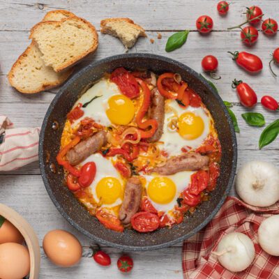 U' funnateglie con uova al tegame, salsicce, pomodori e peperoni in padella