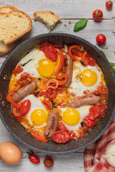 U' funnateglie con uova al tegame, salsicce, pomodori e peperoni in padella