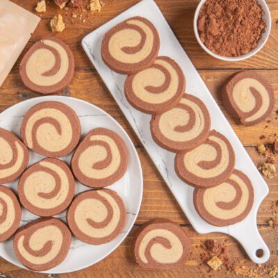 Biscotti maca e cacao a spirale disposti su piatto e tagliere accanto a una ciotola di cacao in polvere