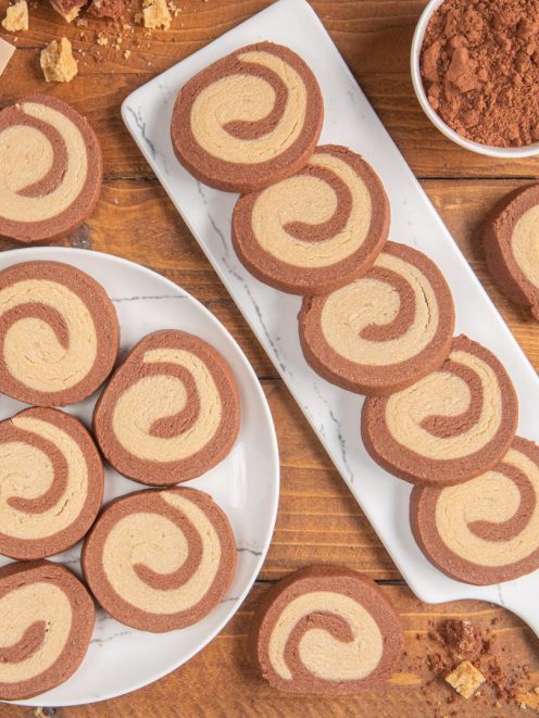 Biscotti maca e cacao a spirale disposti su piatto e tagliere accanto a una ciotola di cacao in polvere