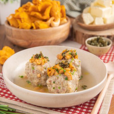 Canederli allo speck in brodo con ragù di finferli, capperi fritti e erba cipollina tritata