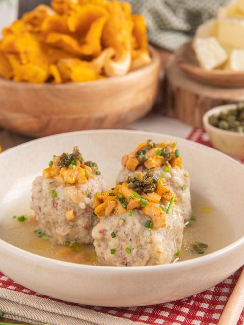 Canederli allo speck in brodo con ragù di finferli, capperi fritti e erba cipollina tritata