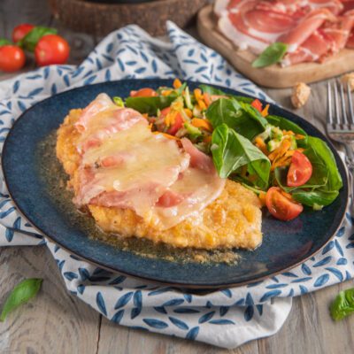 Cotoletta di pollo con fontina fusa e speck, servita con insalata mista e pomodorini