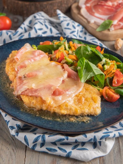 Cotoletta di pollo con fontina fusa e speck, servita con insalata mista e pomodorini