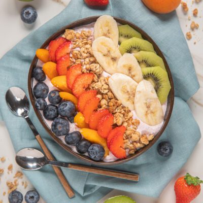 Acai bowl con mirtilli, fragole, pesche, banana, kiwi e granola disposti a strisce colorate