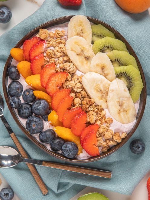 Acai bowl con mirtilli, fragole, pesche, banana, kiwi e granola disposti a strisce colorate