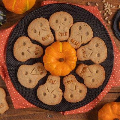 Biscotti teschio di Halloween disposti a cerchio con denti di pinoli attorno a una piccola zucca