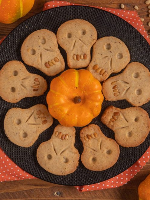 Biscotti teschio di Halloween disposti a cerchio con denti di pinoli attorno a una piccola zucca