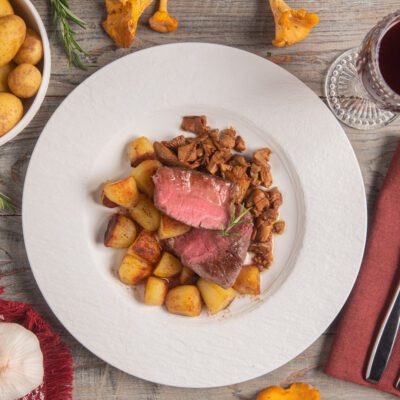 Filetto con riduzione al porto affettato al rosa, servito con patate arrosto e finferli saltati