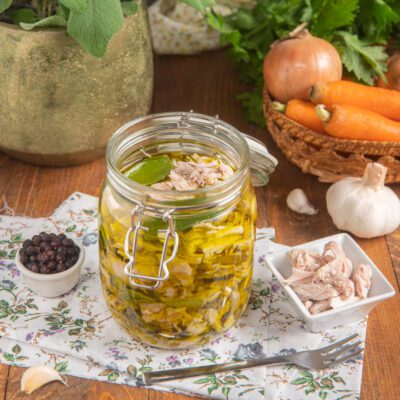 Tonno di coniglio sott'olio in barattolo con alloro, accanto a grani di pepe e aglio