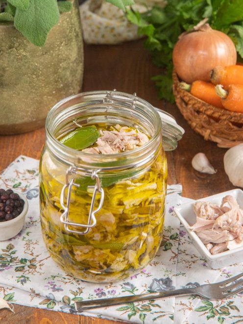 Tonno di coniglio sott'olio in barattolo con alloro, accanto a grani di pepe e aglio
