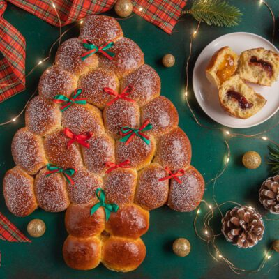 Albero di Natale di Buchteln spolverato di zucchero a velo, con fiocchetti rossi e verdi, farcito con marmellata