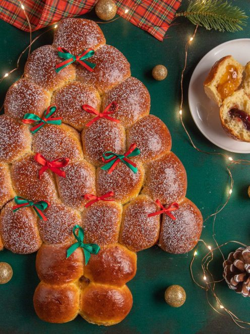Albero di Natale di Buchteln spolverato di zucchero a velo, con fiocchetti rossi e verdi, farcito con marmellata