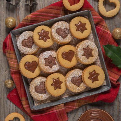 Biscotti ripieni di crema al cioccolato con finestrella a stella e cuore, spolverati di zucchero a velo