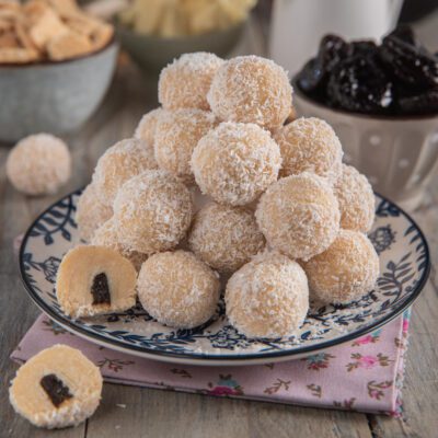 Praline al cioccolato bianco ricoperte di cocco grattugiato con ripieno di prugna, impilate su un piatto