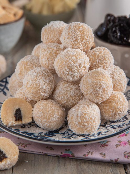 Praline al cioccolato bianco ricoperte di cocco grattugiato con ripieno di prugna, impilate su un piatto