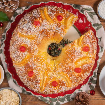 Roscón de Reyes con una fetta tagliata, guarnito con ciliegie candite, mandorle a lamelle e codette di zucchero