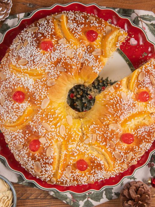 Roscón de Reyes con una fetta tagliata, guarnito con ciliegie candite, mandorle a lamelle e codette di zucchero