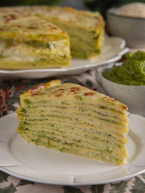 Torta di crespelle con pesto servita a fetta, con strati di verdure e superficie gratinata