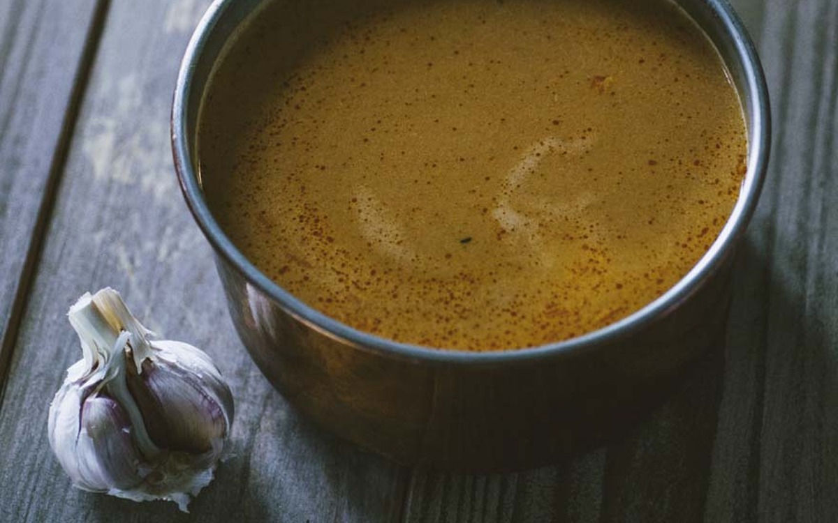 Bisque densa e fumante con spuma dorata in superficie, accanto a una testa d'aglio