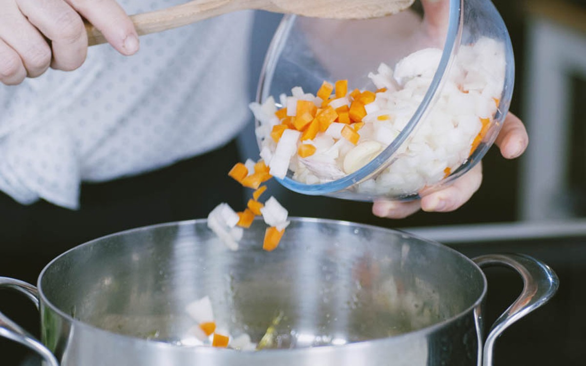 Verdure a dadini di carota e cipolla versate in un tegame per il soffritto della bisque
