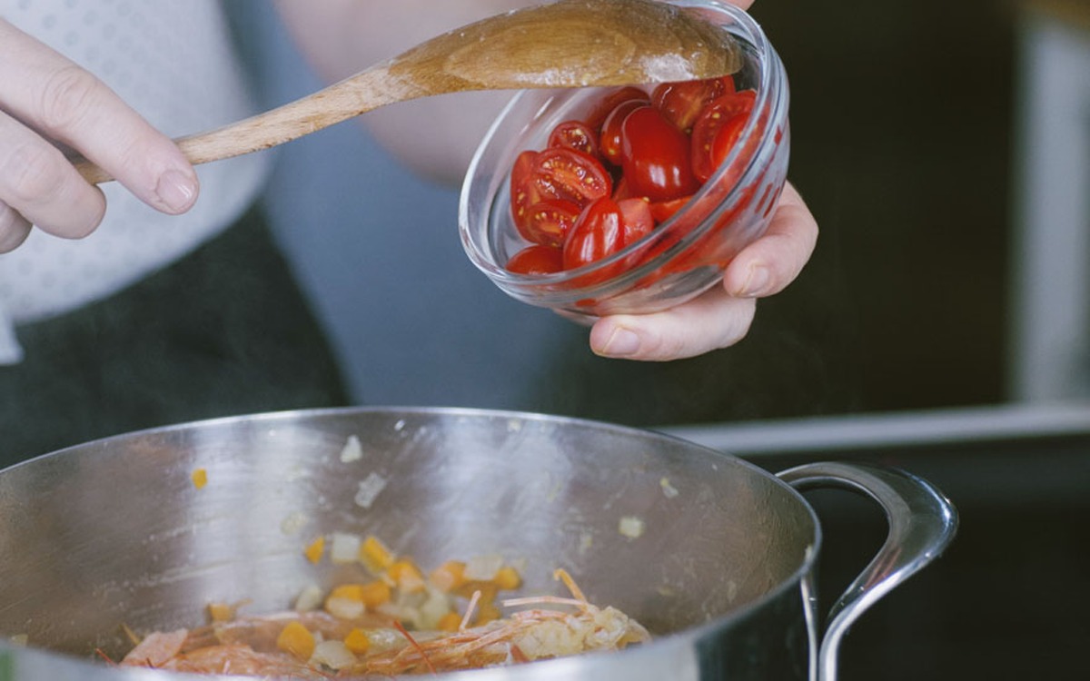 Pomodorini tagliati a metà versati in padella con gamberi e verdure soffritte