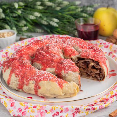 Rocciata umbra a forma di ciambella con glassa rossa e zucchero a velo, ripieno di mele e frutta secca in vista