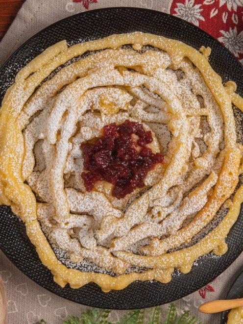 Strauben fritti a spirale spolverati di zucchero a velo con marmellata di mirtilli rossi al centro