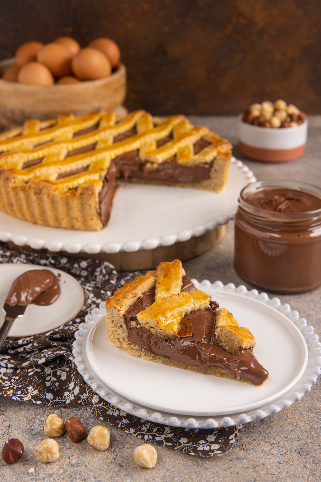 Crostata alla Nutella con reticolo dorato e una fetta servita con ripieno cremoso
