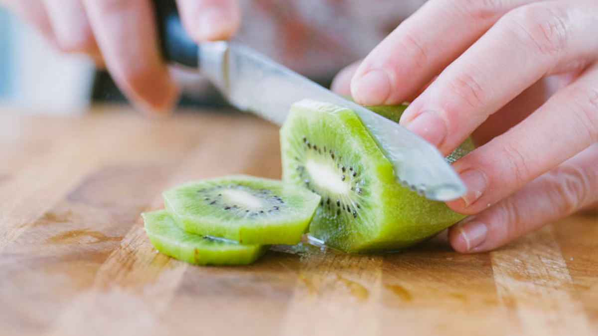 Mani che affettano un kiwi sbucciato su un tagliere di legno