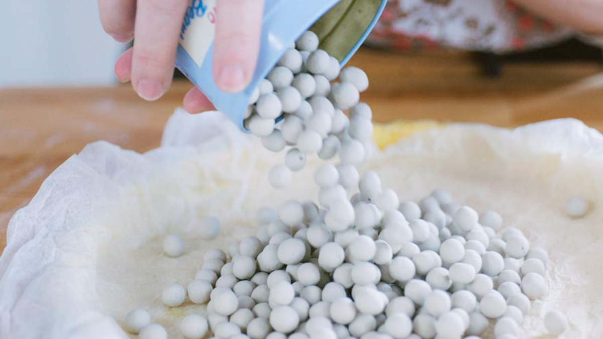 Sfere di ceramica versate sulla carta forno che riveste un guscio di frolla cruda