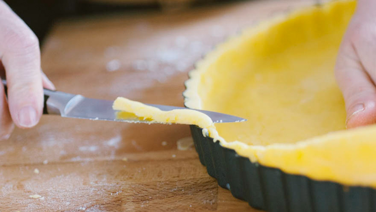 Rifilatura della pasta frolla cruda lungo il bordo dello stampo con un coltellino