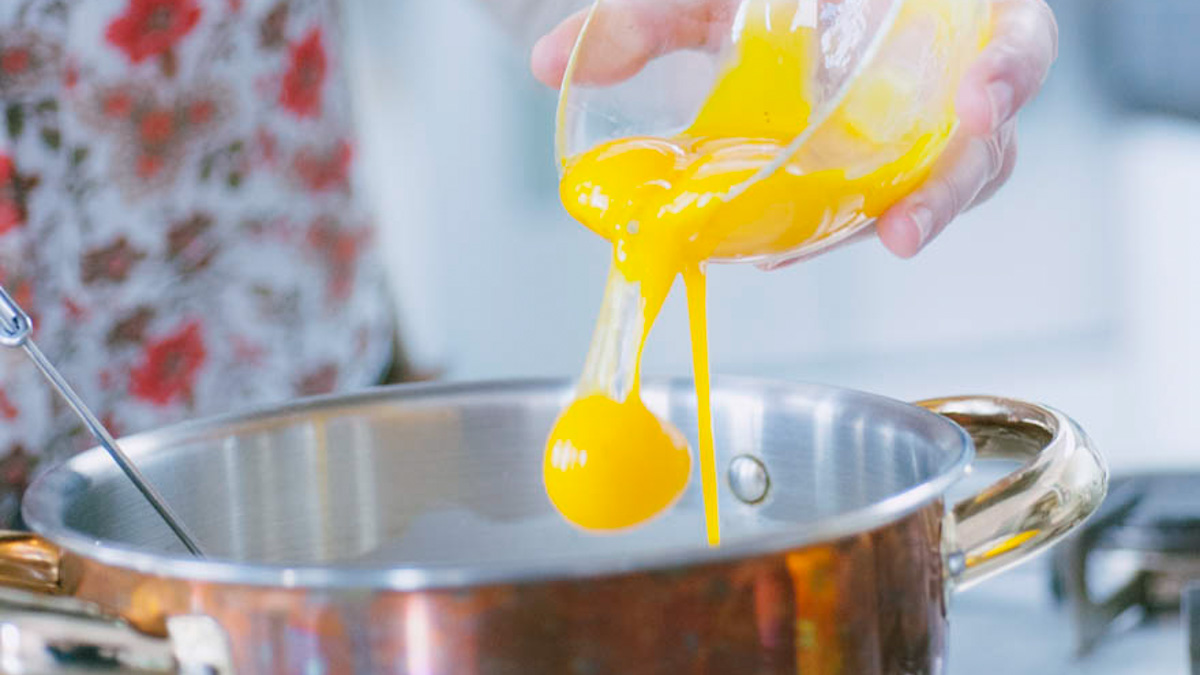 Tuorli d'uovo versati da un contenitore in un tegame per preparare la crema pasticcera