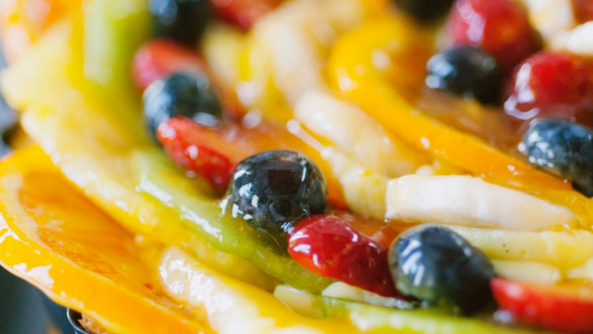 Fette di mango e kiwi con mirtilli e fragole lucidati con gelatina sulla crostata di frutta