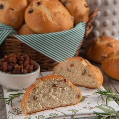 Pane di ramerino spezzato a metà che mostra la mollica soffice con uvetta, accanto ad altri panini dorati