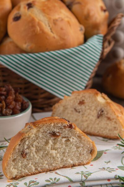 Pane di ramerino spezzato a metà che mostra la mollica soffice con uvetta, accanto ad altri panini dorati