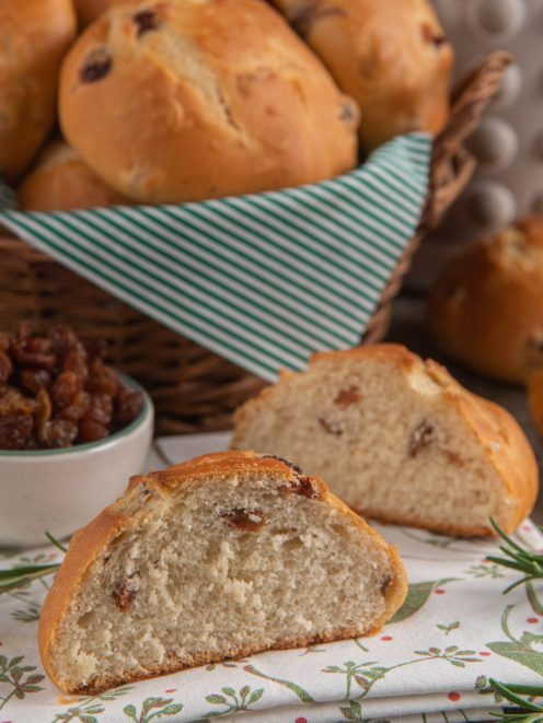 Pane di ramerino spezzato a metà che mostra la mollica soffice con uvetta, accanto ad altri panini dorati