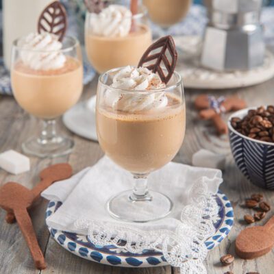 Pannacotta al caffè servita in calice con panna montata e decorazione di cioccolato a foglia