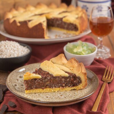 Torta coi bischeri con una fetta servita al piatto, ripieno di cioccolato e pinoli ben visibile