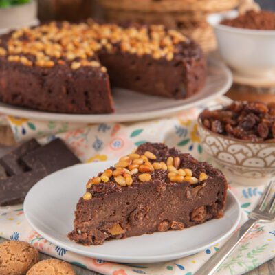 Torta paesana al cioccolato con pinoli in superficie e uvetta nell'impasto, servita a fetta