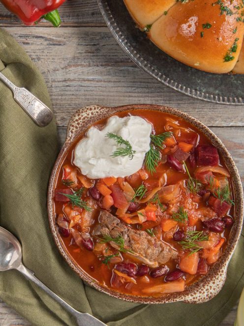 Borscht con carne, barbabietola, fagioli rossi e cavolo, guarnito con panna acida e aneto fresco