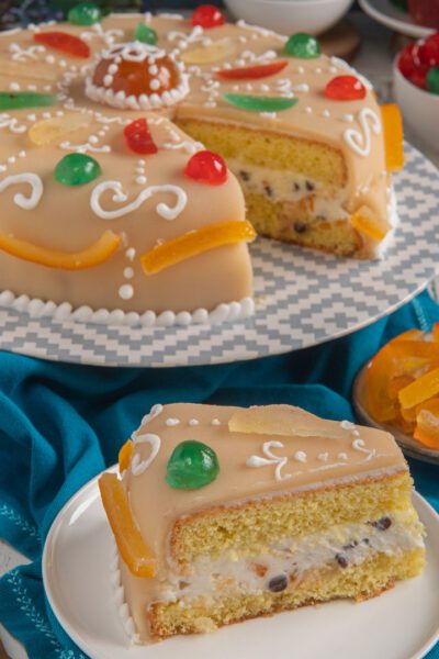 Cassata napoletana con glassa al marzapane, frutta candita colorata e una fetta che mostra il ripieno di ricotta