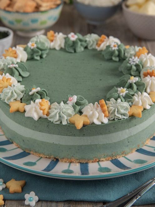 Cheesecake alla spirulina con base di biscotto, ciuffi di crema e decorazioni floreali di pasta frolla