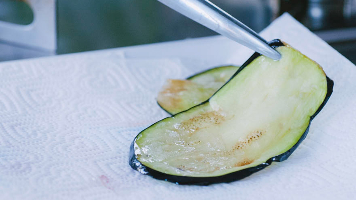 Fette di melanzana fritte scolate su carta assorbente con l'aiuto di pinze da cucina