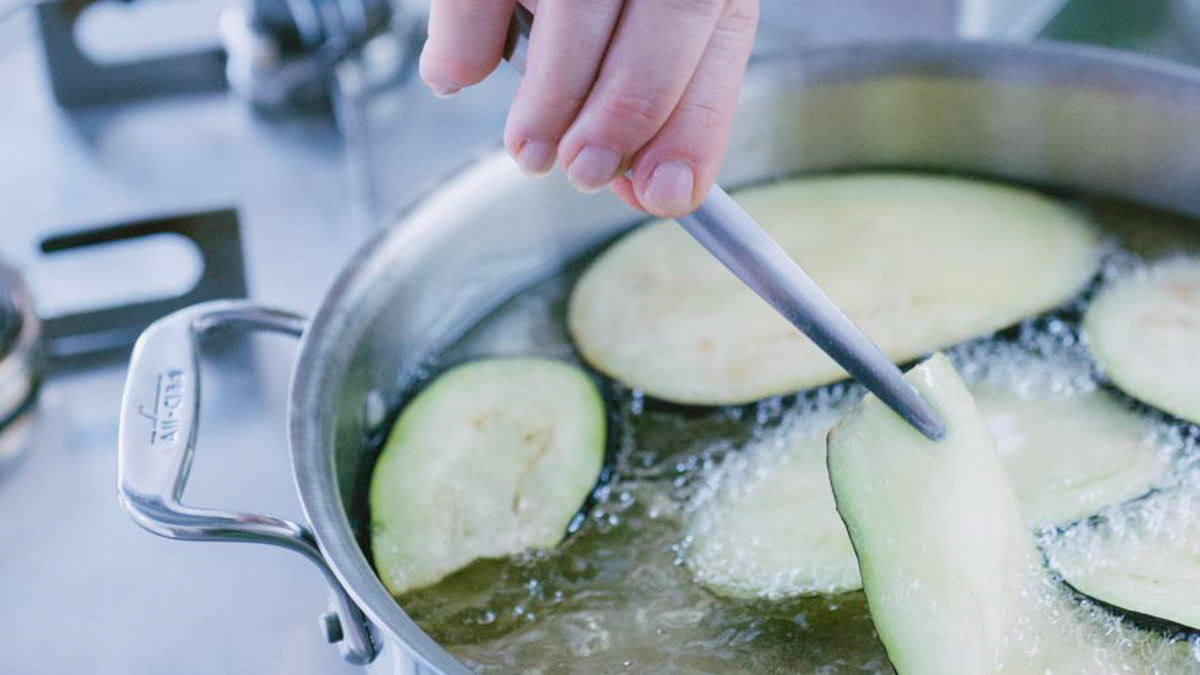 Fette di melanzana che friggono nell'olio caldo, girate con una pinza