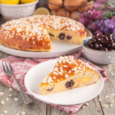 Polacca aversana con una fetta servita in primo piano, crema e amarene nel ripieno, granella di zucchero in superficie