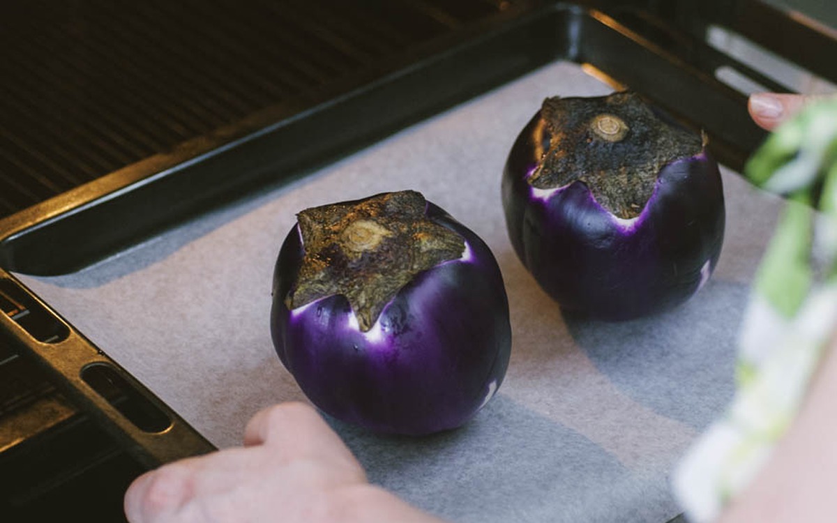 Due melanzane tonde intere disposte su carta forno, pronte per entrare in forno