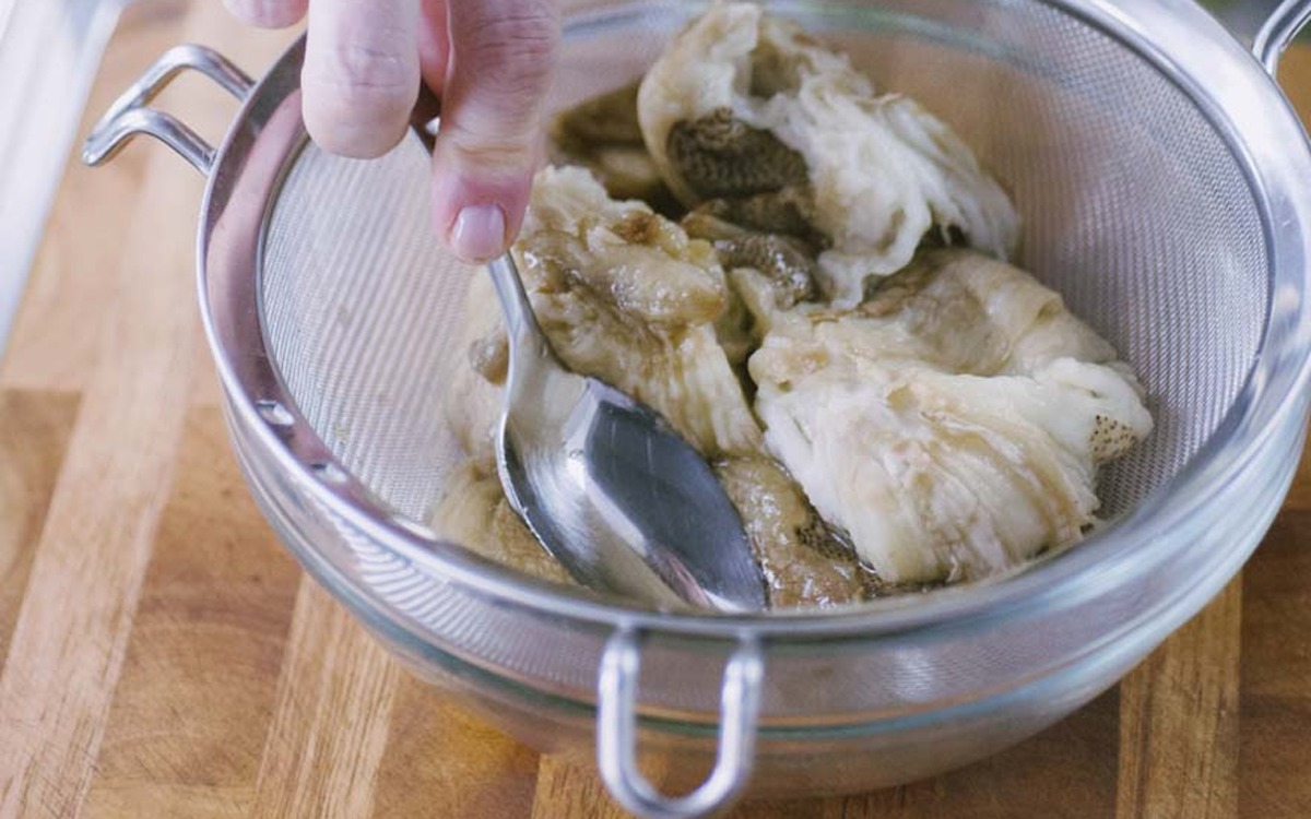 Polpa di melanzane cotta scolata in un colino, pressata con un cucchiaio per eliminare l'acqua in eccesso